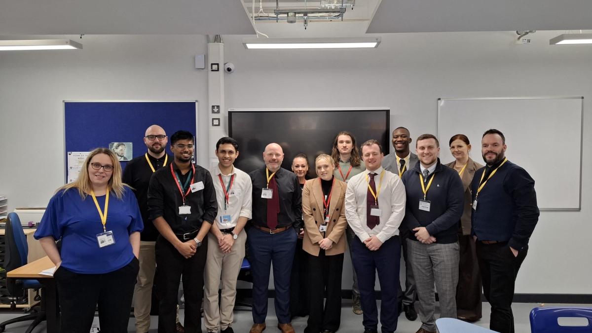 Thirteen people standing in a room in front of a projector screen and whiteboard